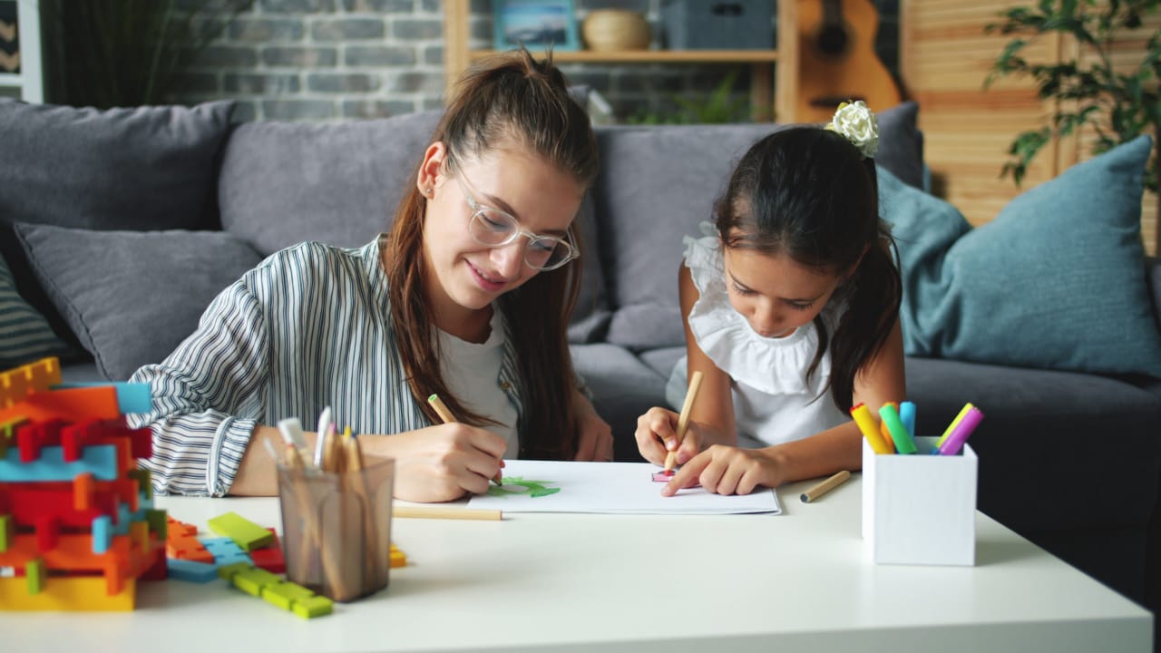 An adult and a child drawing a plan together with pencils at a table